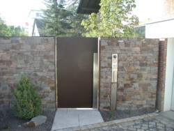 Cortenstahltüre mit Edelstahlstoßgriff mit seitlicher Funktonssäule in der Natursteinmauer.